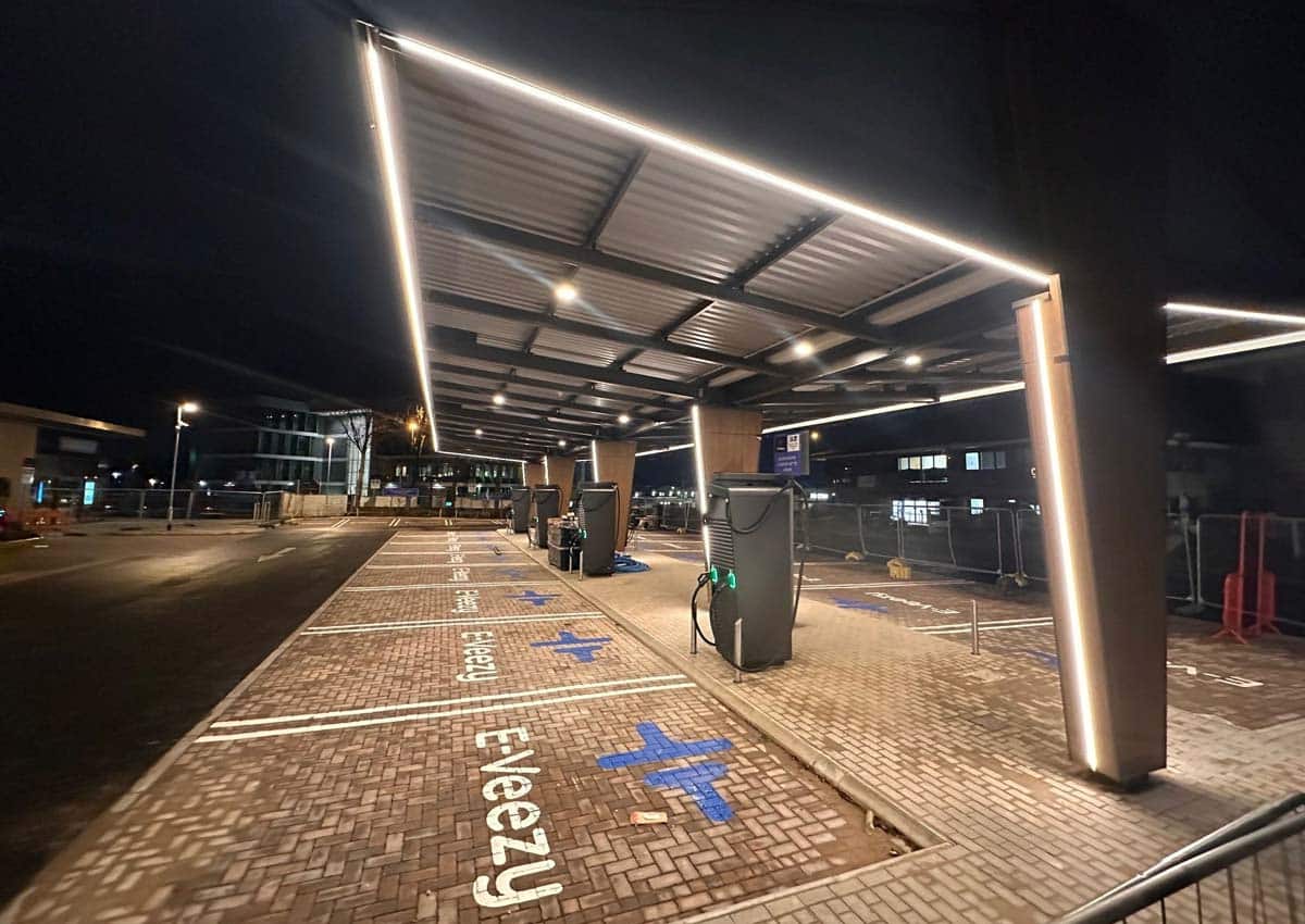 Electric vehicle charging station at night with multiple ultra‑rapid chargers under a lit canopy at the new E‑Veezy site in Manor Royal.